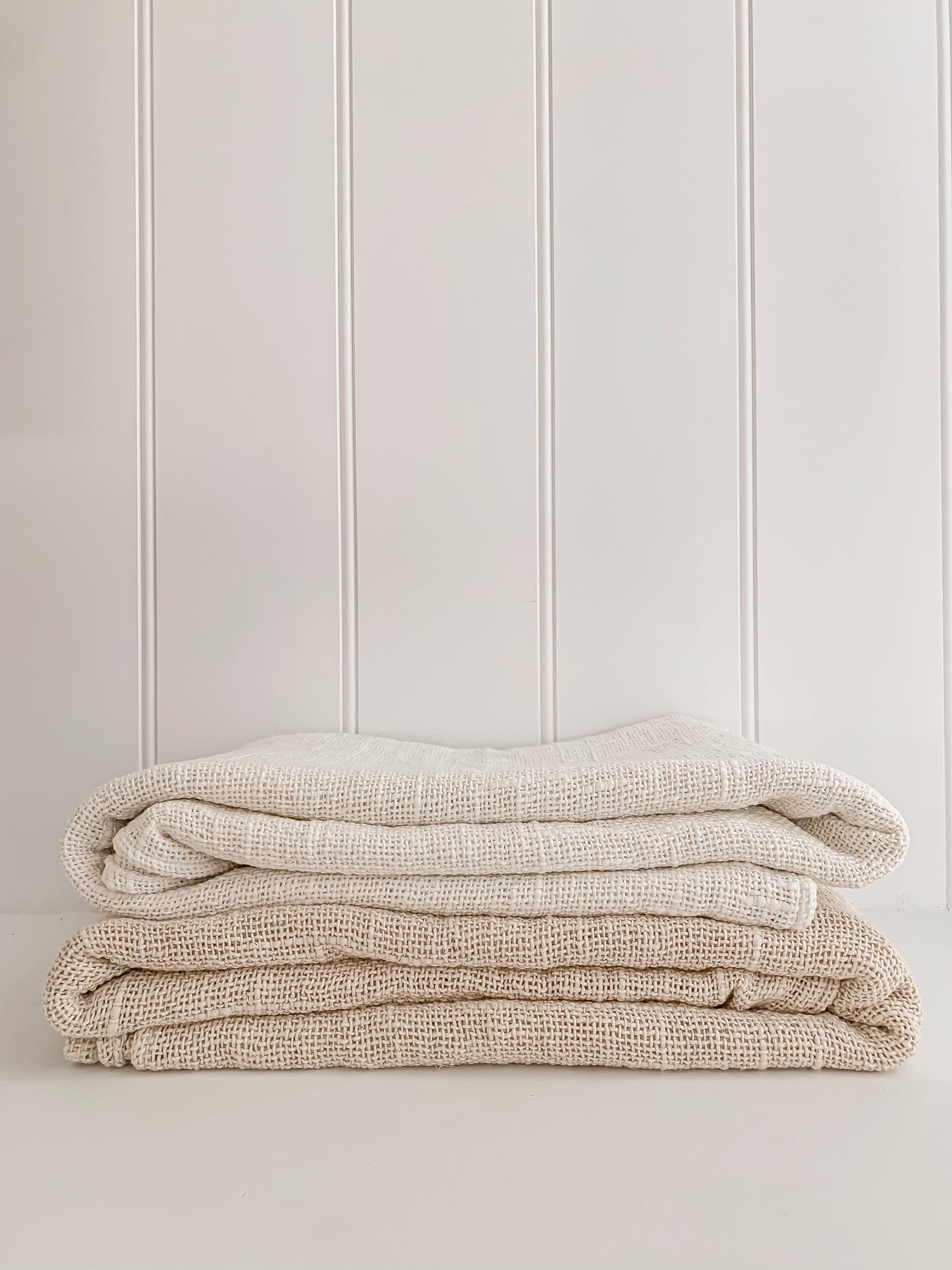 A stack of handcrafted white and natural Barre Living Linen Throws against a white wall.