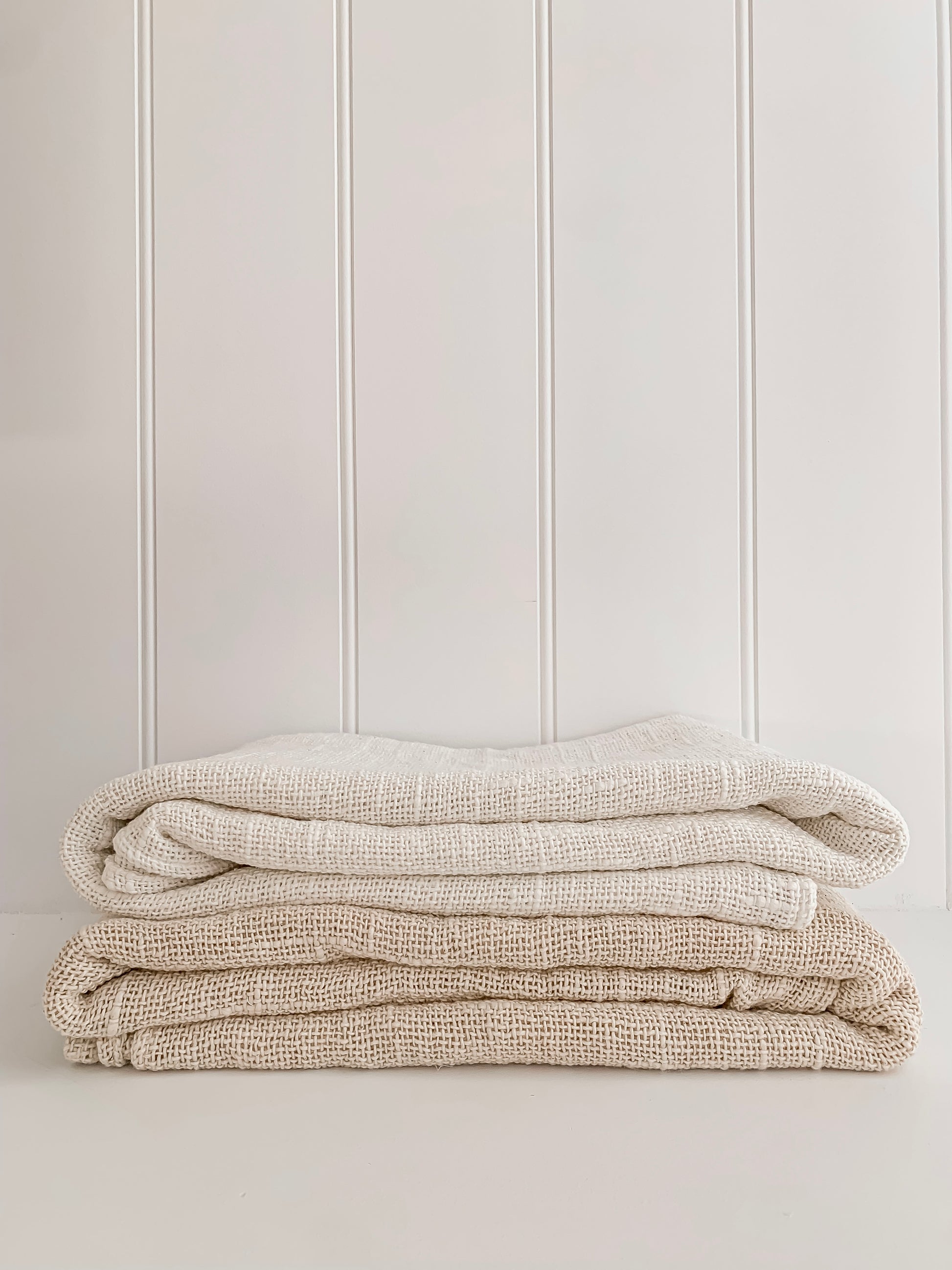 A stack of handcrafted white and natural Barre Living Linen Throws against a white wall.