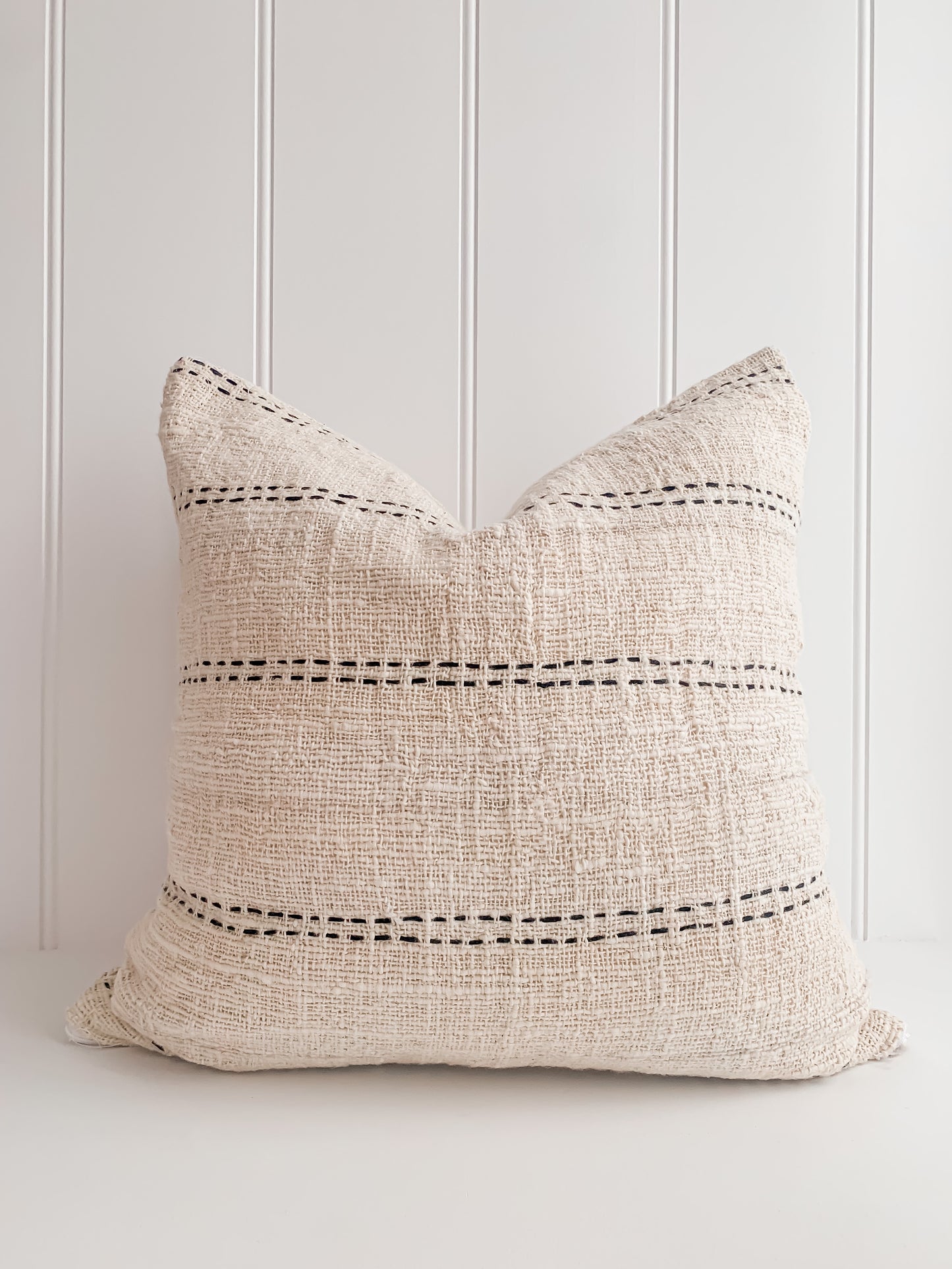 A simple Nyah | Stitch Cushion with natural colors on a white surface.