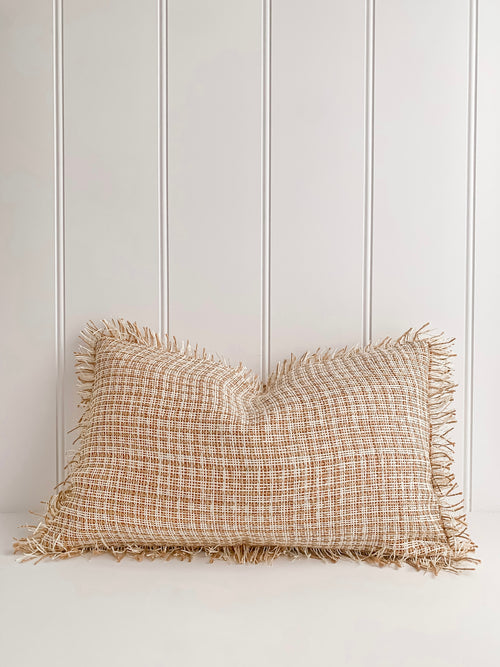 A beige Ava | Weave cushion with elegant fringes sitting on top of a white wall.