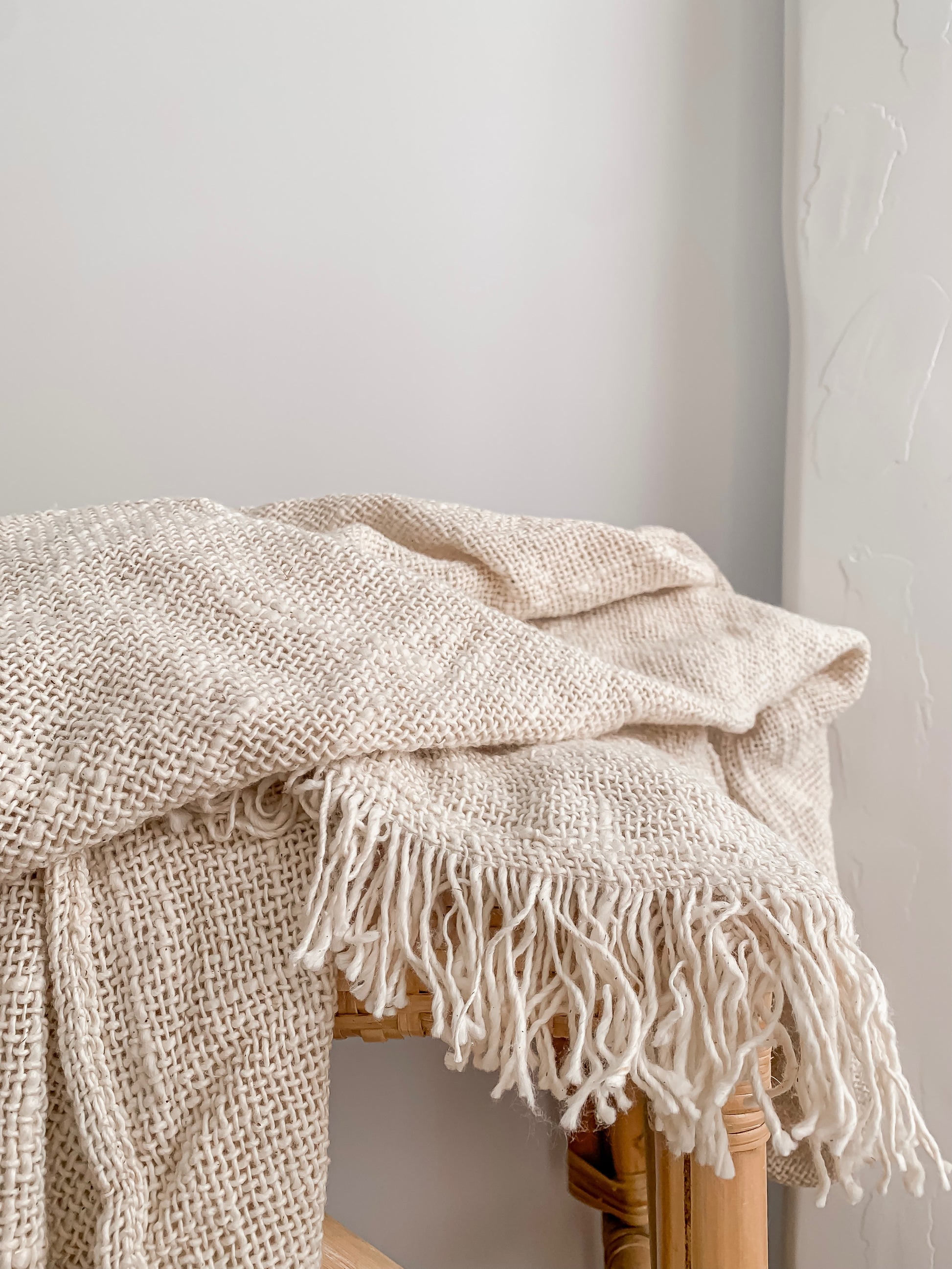 A handcrafted Arlo Throw with fringes on top of a wooden chair by Barre Living.