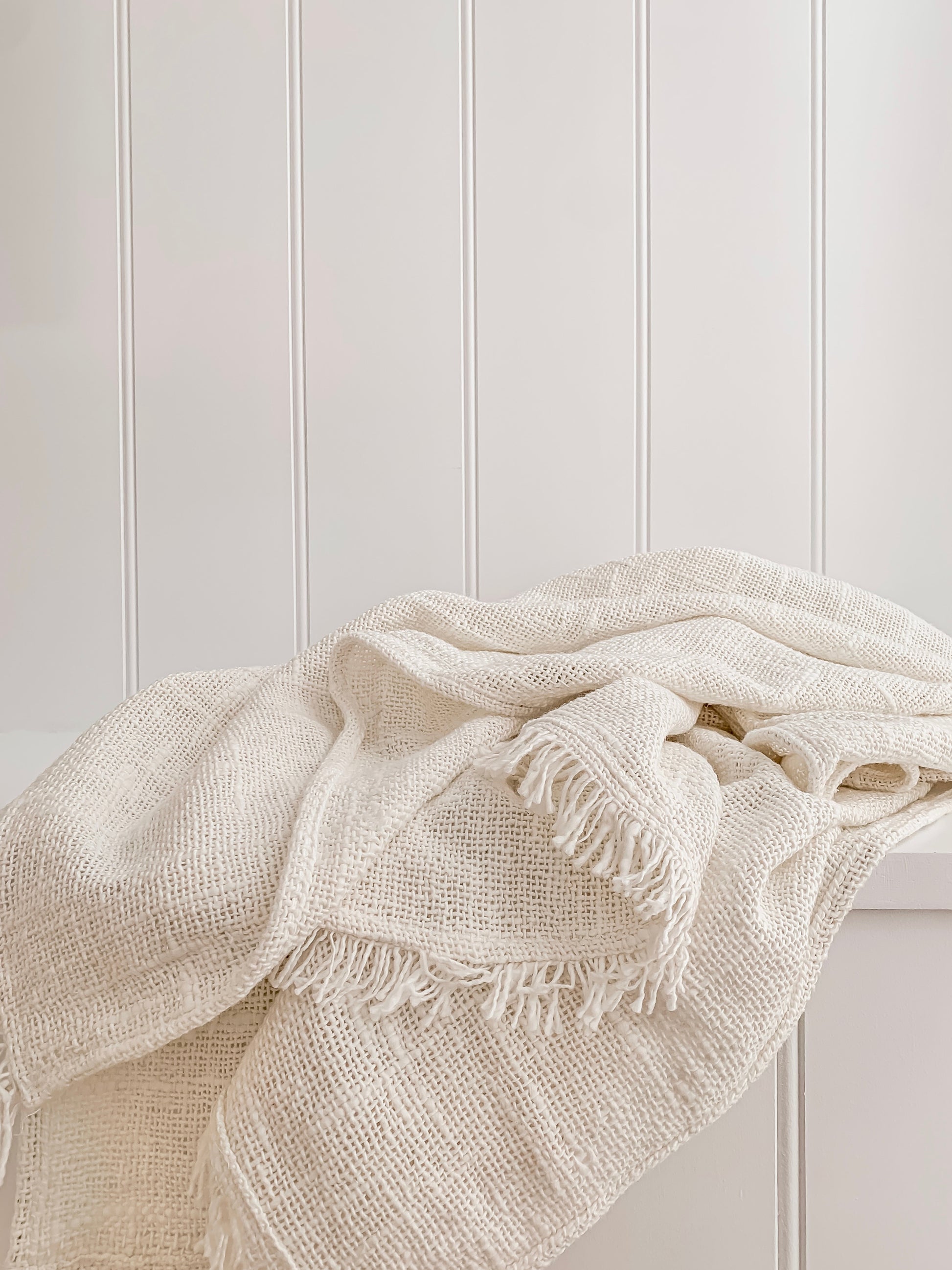 A Barre Living Arlo Handcrafted Linen Throw with fringes on top of a white wall.