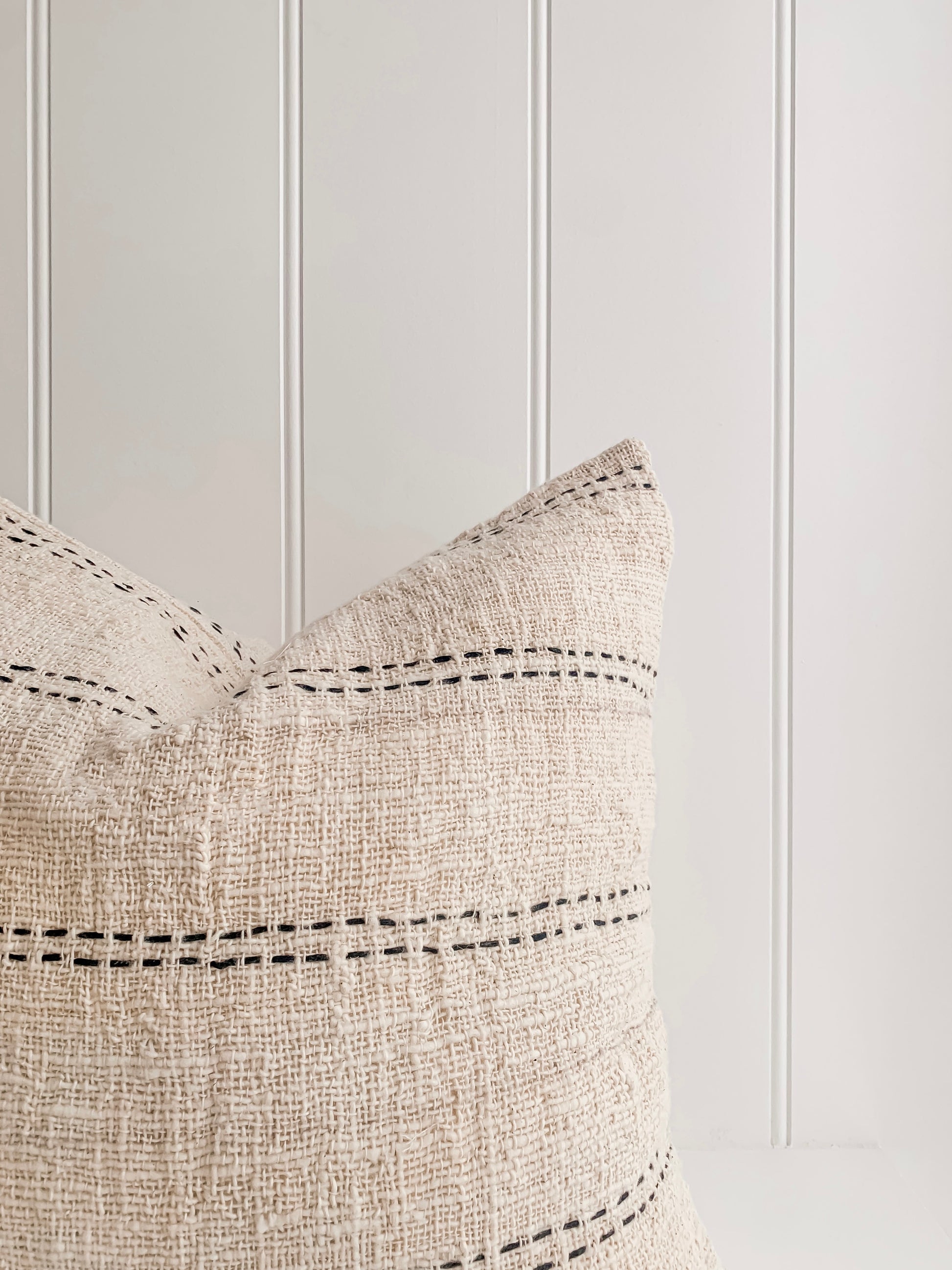 A beige and black striped Nyah | Stitch Cushion cover on a white table by Barre Living.