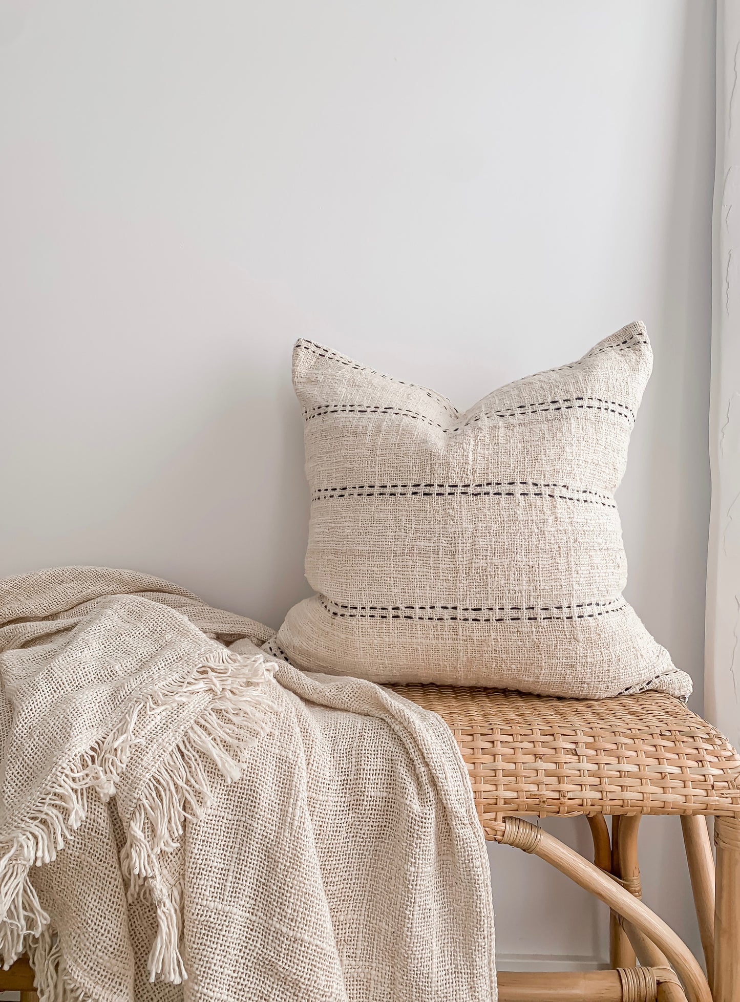 A Nyah | Stitch Cushion wicker bench with a simple patterned blanket. Brand: Barre Living.